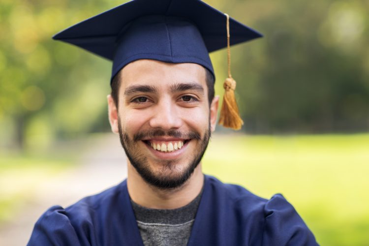 education, graduation and people concept - close up of happy student in mortar boards and bachelor gown outdoors